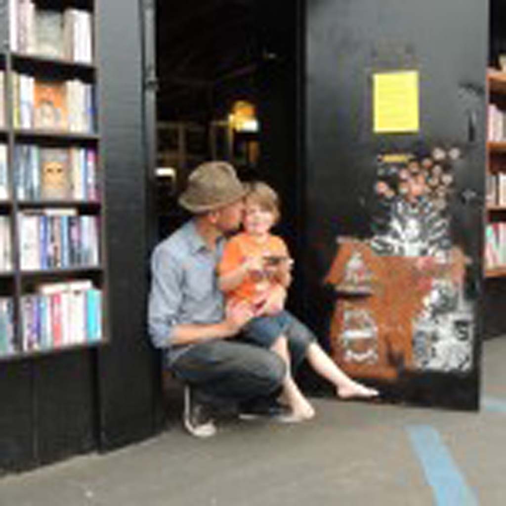 Sean Christopher holds his 4-year-old son, Jack, outside of the free bookstand he set up outside of his bookstore, L.H.O.O.Q. Books, in Carlsbad Village. Photo by Rachel Stine