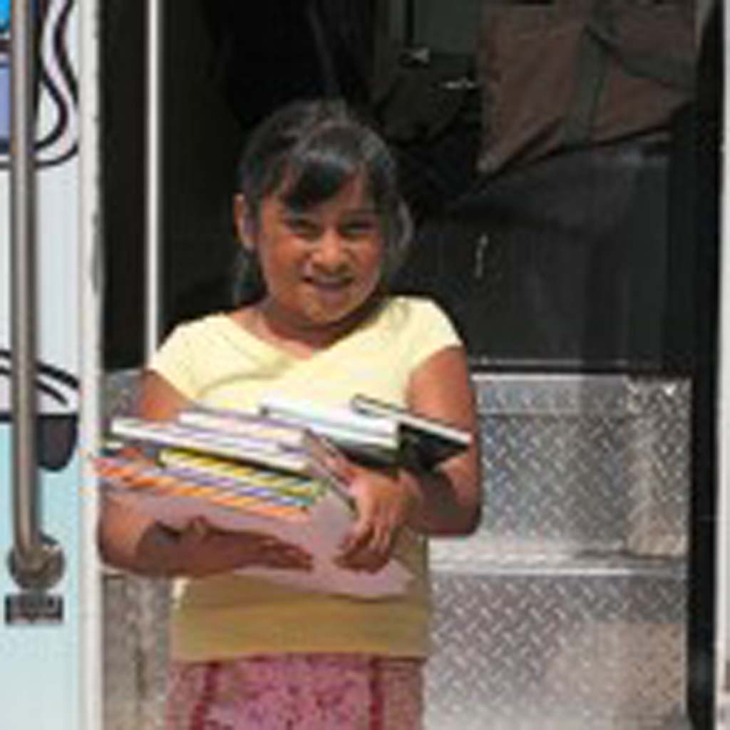 Leslie Garcia, 7, of Oceanside, checks out an armful of books. The Adelante Bookmobile will serve an estimated 10,000 people a year. Oceanside will add a second bookmobile and three more stops to its outreach service. Photo by Promise Yee