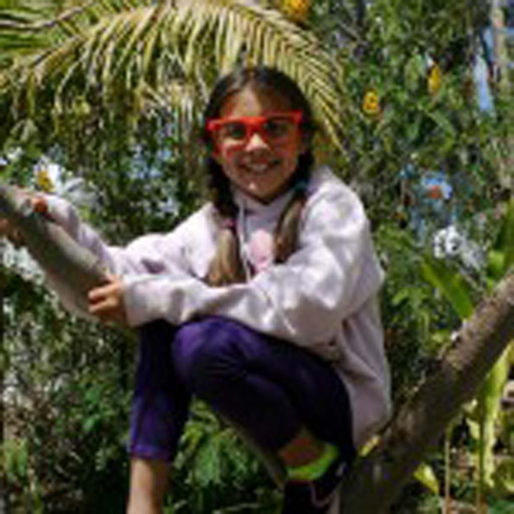 Isabella Castillo, 11, of San Marcos, enjoys the view from a garden tree. The gardens boast 80 types of fruit trees and vegetables. Photo by Promise Yee