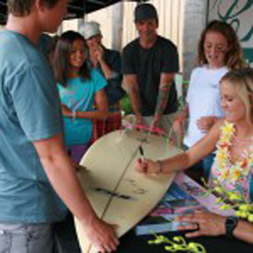 Isabella Darisay, 12, of Carlsbad, left, and Chloe Pierson, 12, of Oceanside stand by as Bethany Hamilton signs Chloe’s surfboard. Fans lined up around the block to meet Hamilton on July 19. Photo by Promise Yee
