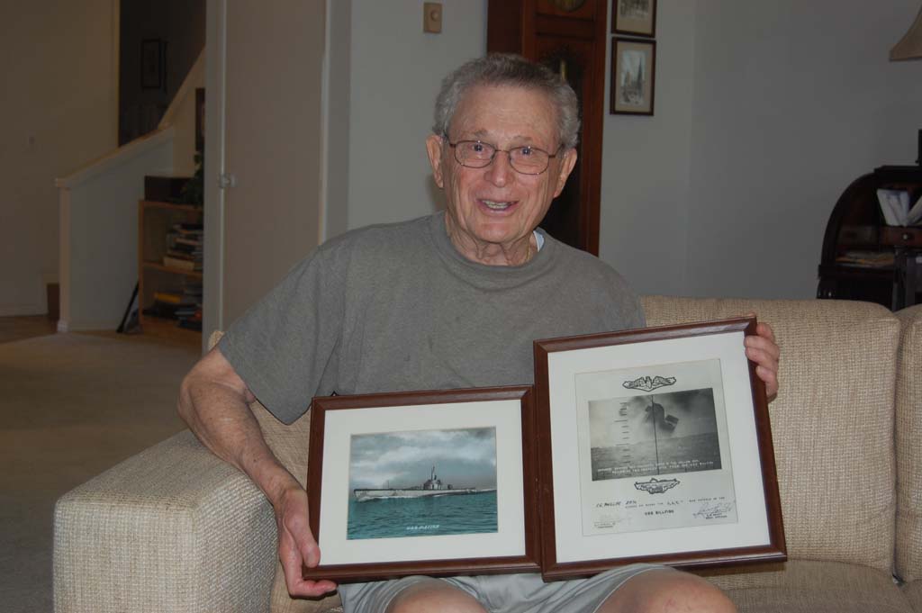Seymour Phillips, 89, displays some of his World War II photos. The one on the right shows a Japanese freighter following two torpedo hits from the USS Billfish, on which Phillips served. Photo by Bianca Kaplanek