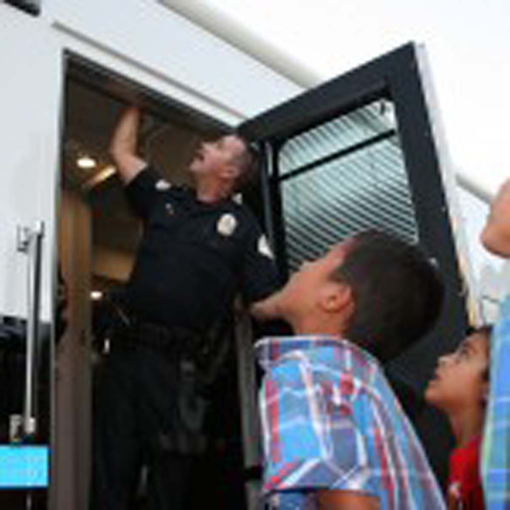 Children watch as Officer Robert Sarracino adjusts the rooftop camera on the police mobile command center. Then they follow him inside for a tour of the mobile station. Photo by Promise Yee