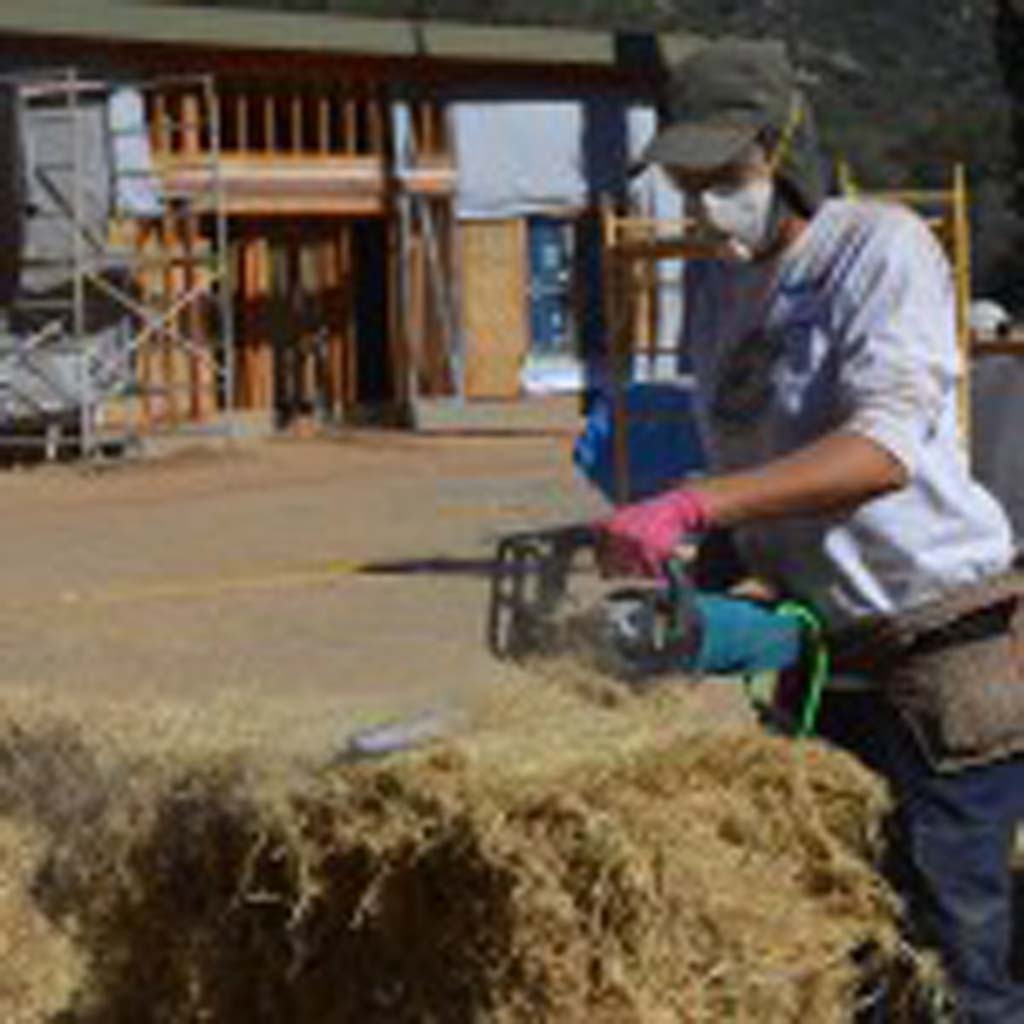 A chainsaw is used to cut into a straw bale that will eventually be placed into the wooden frames and become the walls of new housing for the Zen Buddhist nuns at Deer Park Monastery in Escondido. Photo by Tony Cagala