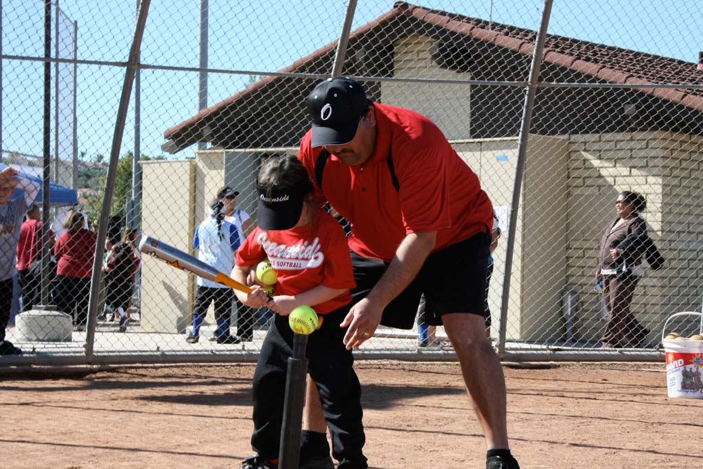 A volunteer coach helps first time hitter strike the ball at previous year’s Opening Day games. Opening Day celebrations for Oceanside leagues will include introducing teams, fundraising booths, and first games. Photo by Promise Yee