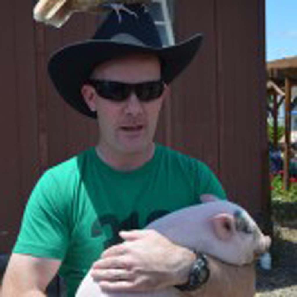 Ian McDuffie holds a baby pig while a Polish hen sits on his head. Photo by Tony Cagala