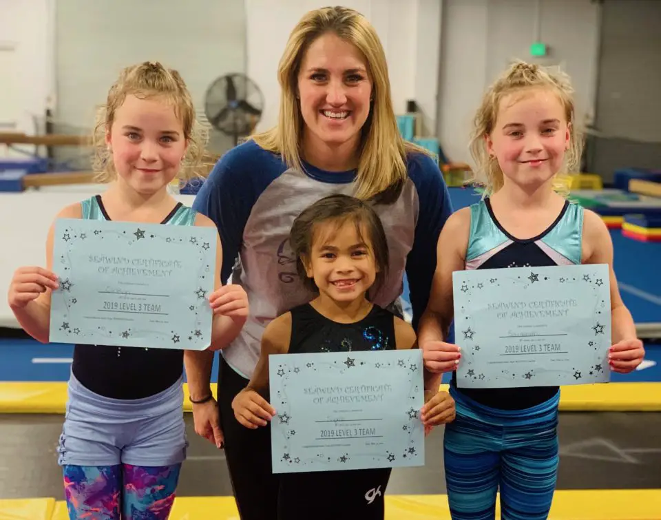 Lydia Jo Budny stands behind gymnastic students holding up awards