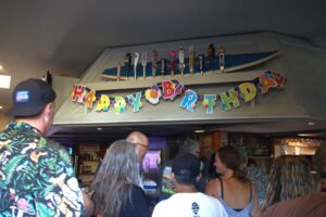Family, friends and longtime customers of the Tidewater Tavern in Solana Beach celebrate owner Sam Lunde’s birthday ahead of the business’s closing in early September. Photo by Laura Place