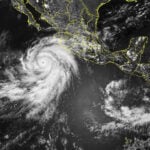 In this visible satellite picture, clouds are white, the ground is normally grey, and water is dark. The eye of Hurricane Hilary can be seen just south of the Baja California Peninsula. Photo courtesy of NOAA
