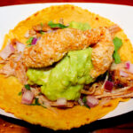 Slow-cooked pork carnitas topped with cilantro, onion, guacamole, topped with a crunchy pork rind. Photo by Rico Casson