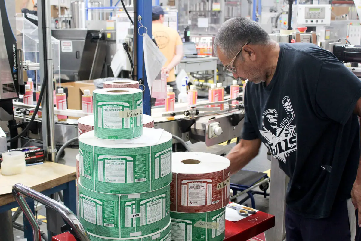 Rotary production worker Marcus Yepiz manages the labeling of Dr. Bronner’s liquid soap bottles at the company’s Vista factory. Photo by Laura Place