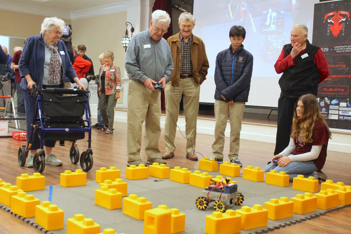 Members of the Tri-City Christian High School Robotics Team demonstrate how to run the “baby bot” through a maze to residents at La Costa Glen on Tuesday. Photo by Laura Place