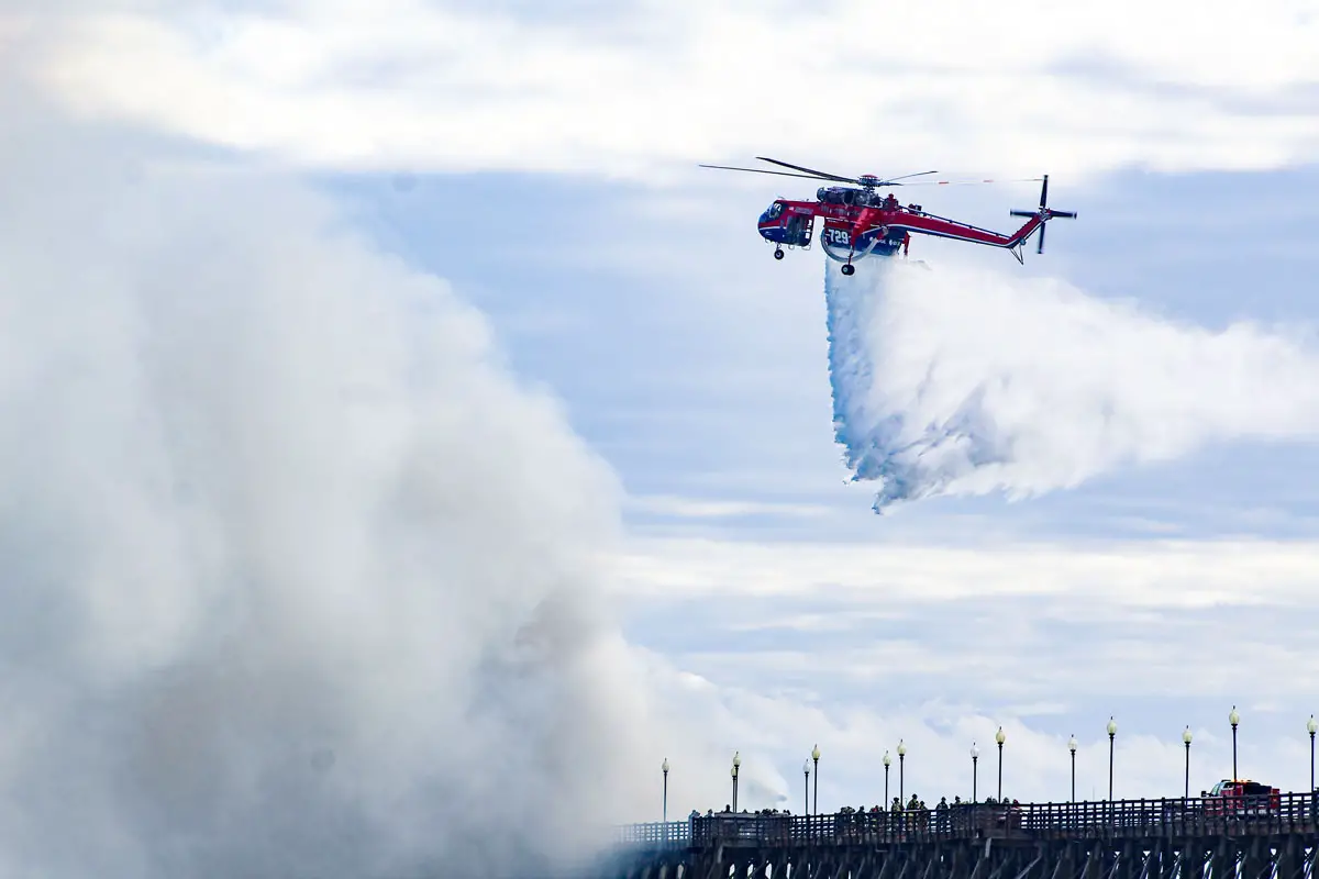 A helicopter owned by SDG&E drops ocean water onto the fire on Thursday evening at Oceanside Pier. Photo by Samantha Nelson