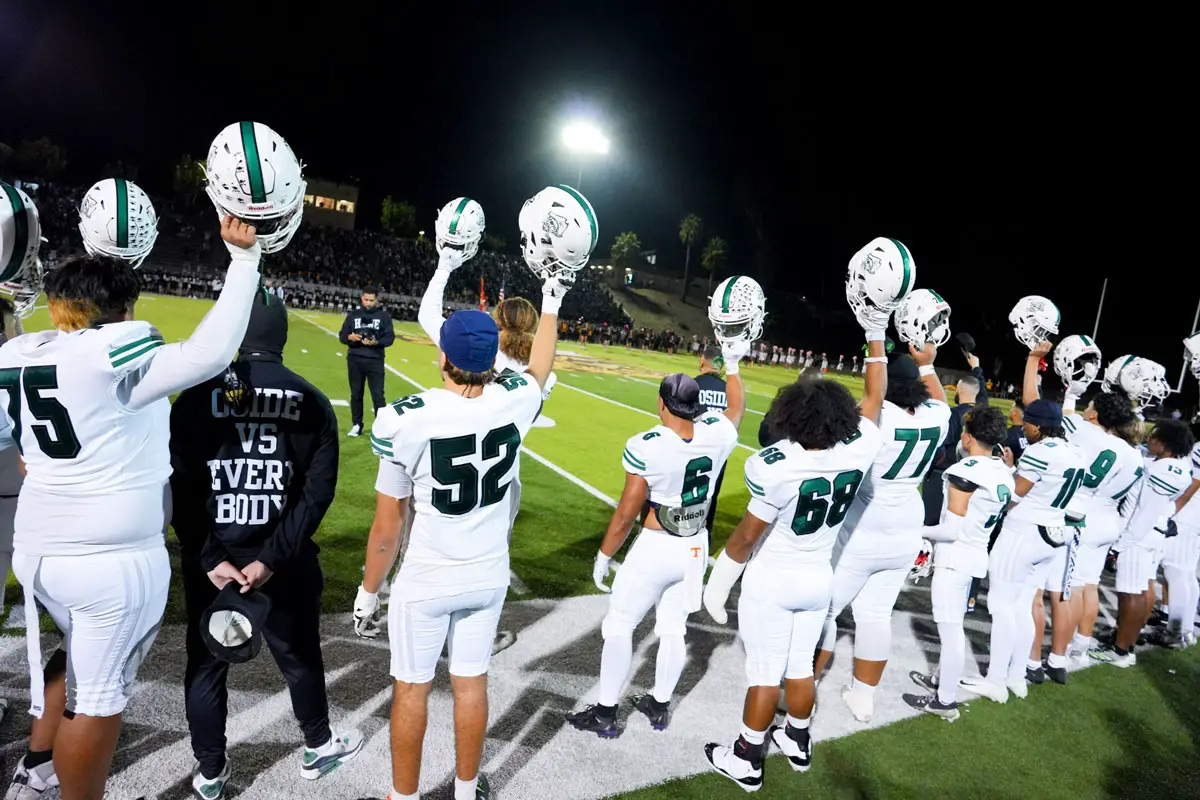 Oceanside players raise their helmets on the sideline late in the Battle of Oceanside rivalry game on Oct. 30 at Herb Meyer Stadium. The Pirates secured the Avocado East League title and capped a 6-4 regular season with a 22-0 shutout over crosstown rival El Camino. Photo by Lajos Kamocsay