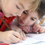 Young girl writes in notebook as another girl looks on.