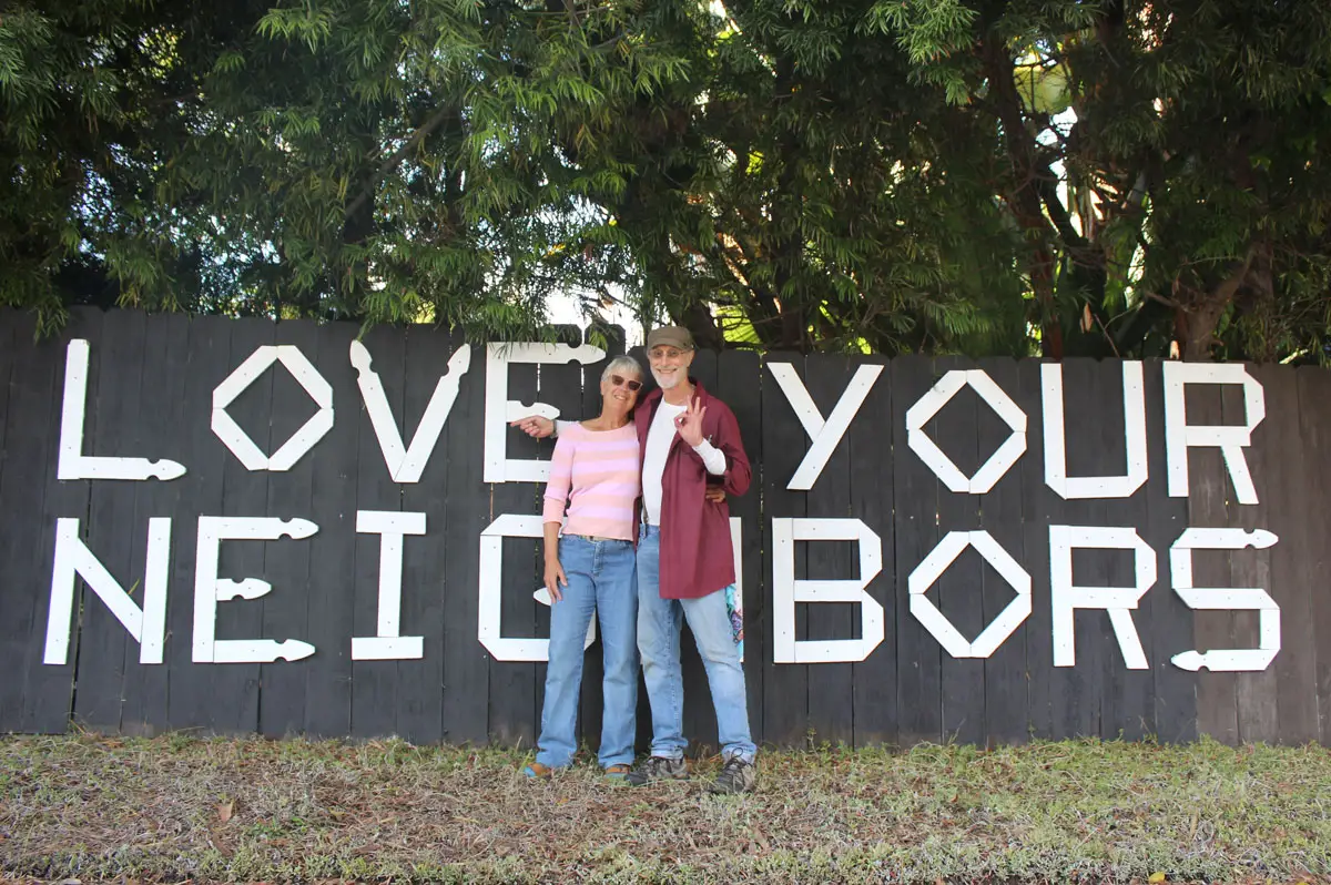 JT Moring and his wife, Mary Jo Preti, pose in front of the wooden “Love Your Neighbors” letters on Nov. 21, 2025, in Encinitas. The couple says the community has overwhelmingly supported keeping the sign after the city issued a violation notice. Photo by Jordan P. Ingram