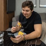 Young man eating breakfast while using smartphone at kitchen table