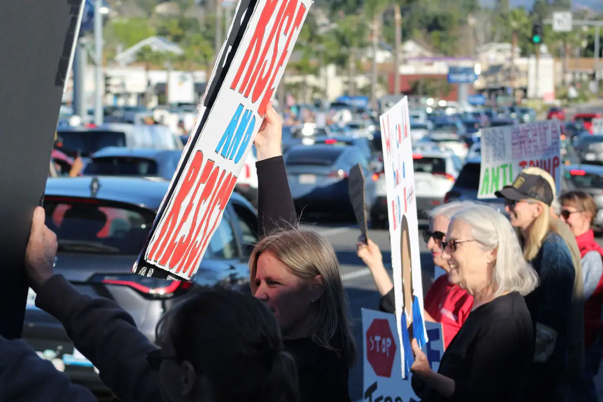 Protesters line a busy intersection holding signs during an “ICE Out For Good” demonstration in Encinitas. Photo by Cameron Adams