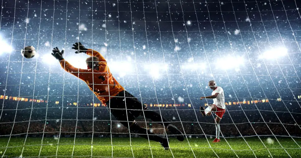 Goalkeeper diving to block a shot during a professional soccer match under stadium lights