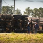 A commercial truck lies on the side of the road after an accident as safety workers gather.