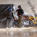 two men stand near a homeless encampment under the Interstate 15 overpass at El Norte Parkway in Escondido. Photo by Frank Armstrong