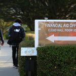 Students walk past a sign for a campus financial aid office on Dec. 8, 2017. Photo By Lea Suzuki, The San Francisco Chronicle via Getty Images