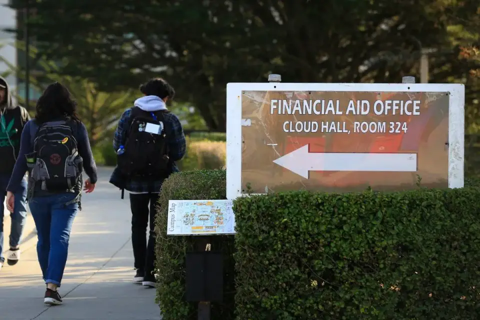 Students walk past a sign for a campus financial aid office on Dec. 8, 2017. Photo By Lea Suzuki, The San Francisco Chronicle via Getty Images