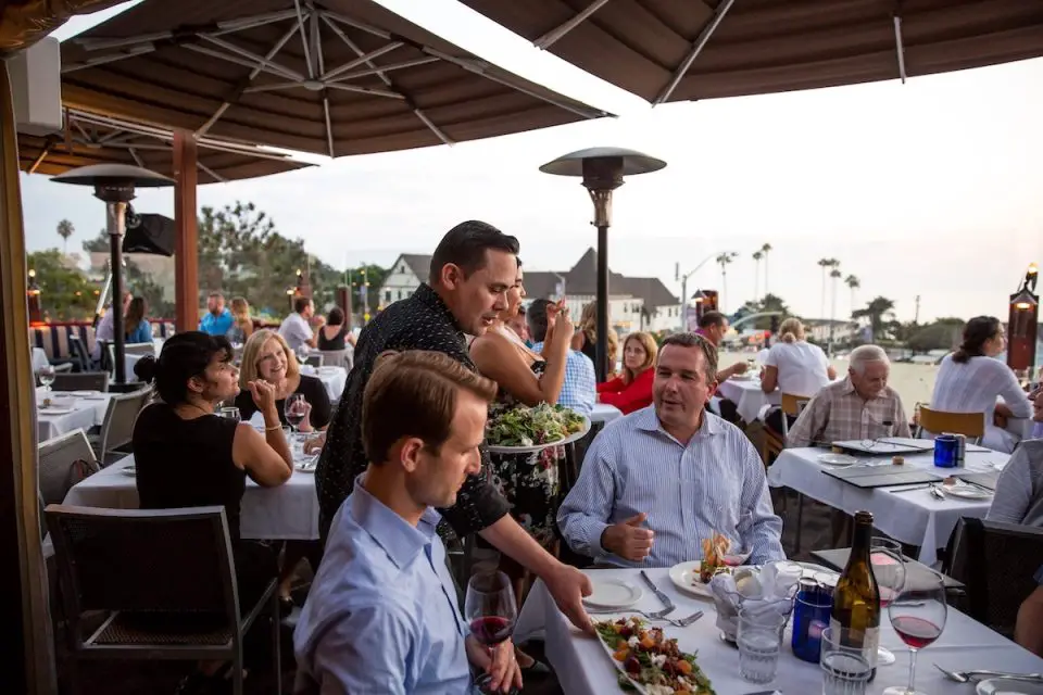 A server brings food to a table where two men are sitting on a balcony.