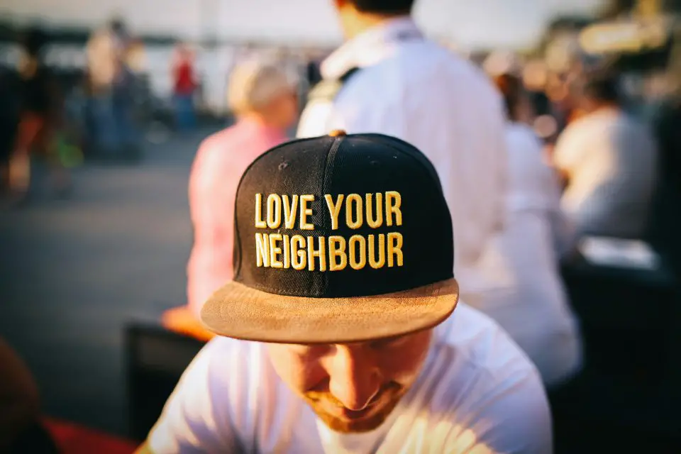 Person wearing a "Love Your Neighbour" hat at a community gathering, representing community investment and neighborhood development.