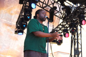 A man in a green shirt speaks into a microphone on a stage.