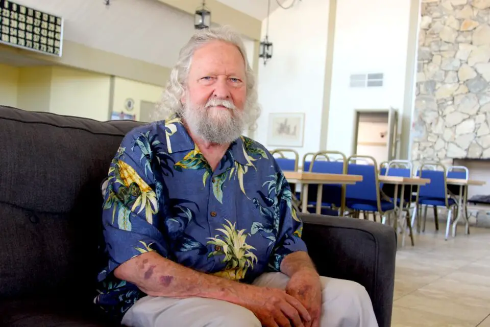 A man with white hair and a white beard sitting on a couch