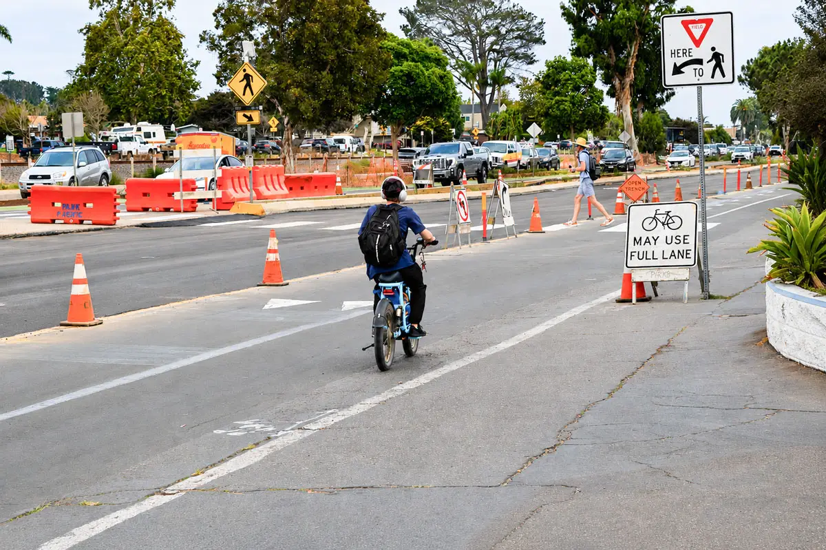 Construction signs, orange barricades and traffic cones line North Coast Highway 101 in Leucadia as a cyclist and pedestrian pass through the corridor during the Leucadia Streetscape project. Photo by Summer Hu