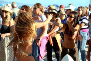 Two girls dance on the beach in a crowd