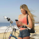 Woman checking her smartphone beside a bicycle overlooking a Southern California beach