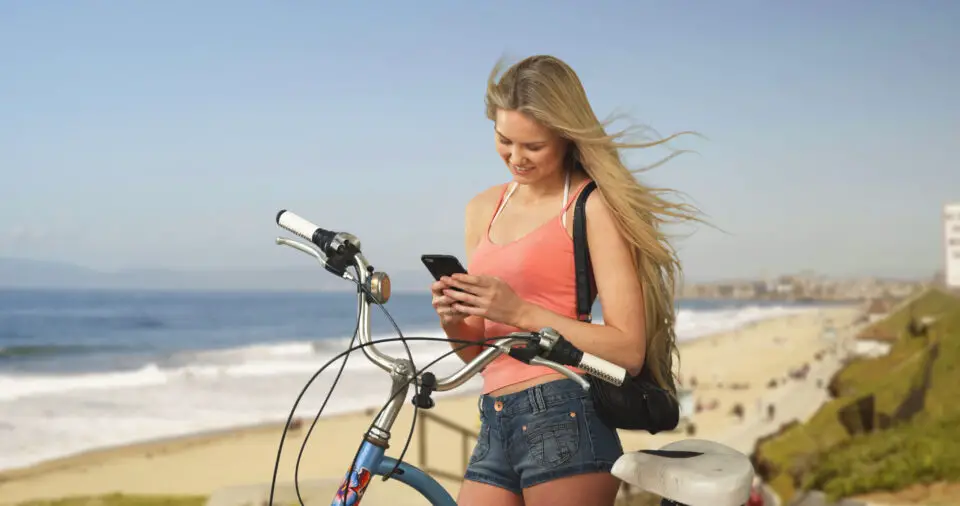 Woman checking her smartphone beside a bicycle overlooking a Southern California beach