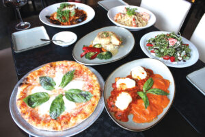 A collection of Tommy V’s extraordinary entrees: Clockwise from top, Francisco’s Seafood Brodetto, Fettucine Carbonara with shrimp, Arugula Salad, Parmigiana with lobster ravioli, Margherita pizza and Halibut Fish of the Day. Photo by Rico Cassoni