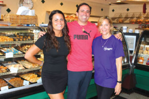 Servers Gina Stravinsky, left, and Karen Goldstein flank managing partner Gil Frank in front of Milton’s bakery cases. Photo by Rico Cassoni