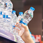 A customer grabs a plastic water bottle from a grocery store shelf.