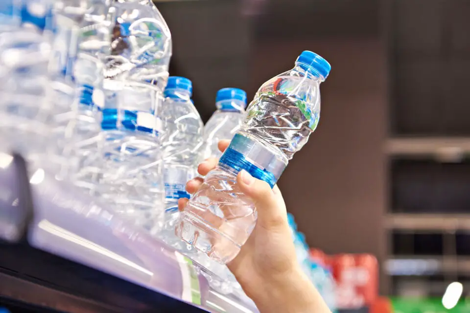 A customer grabs a plastic water bottle from a grocery store shelf.