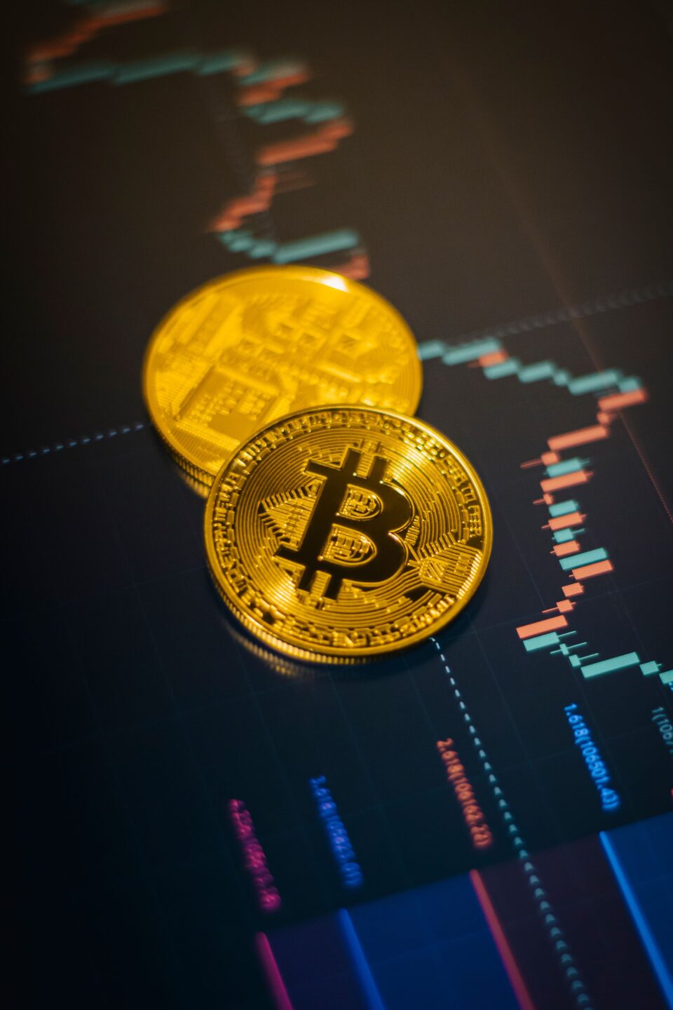 Two gold-colored Bitcoin tokens resting on a screen displaying a financial trading chart.