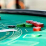 Stacks of red, green and black casino chips beside playing cards on a green felt gaming table.