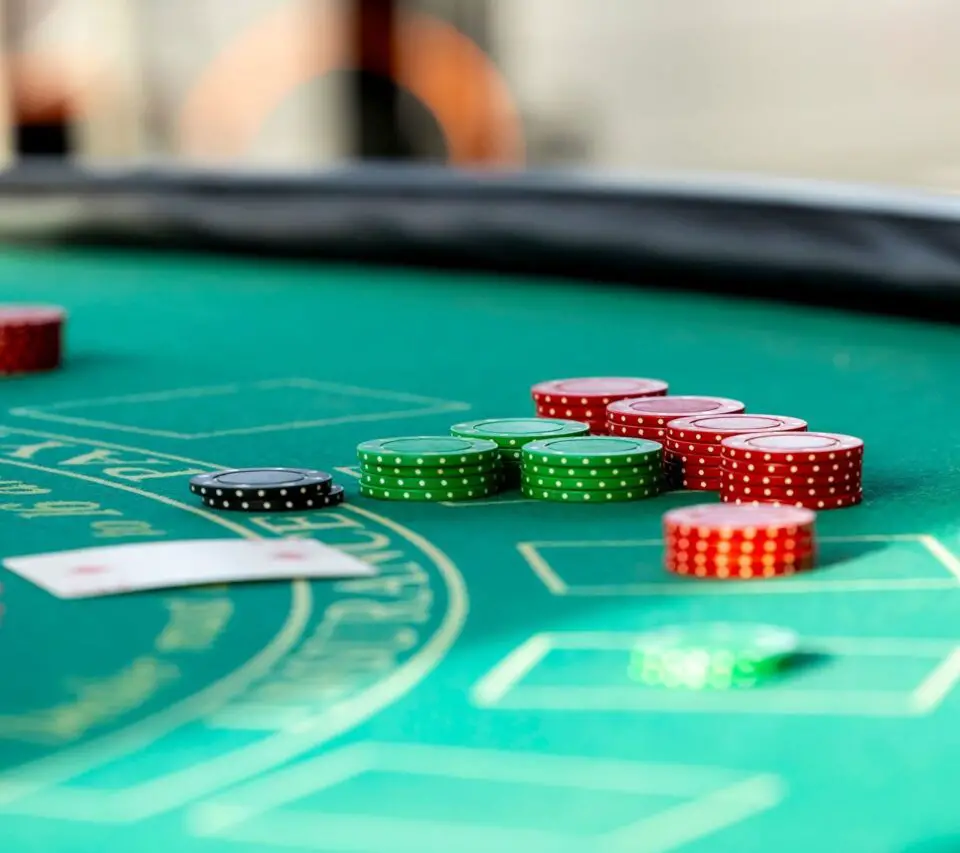 Stacks of red, green and black casino chips beside playing cards on a green felt gaming table.