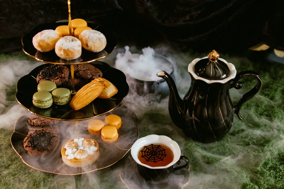 Tiered pastries beside a black teapot and spiderweb teacup in a misty Halloween display at Four Seasons Aviara in Carlsbad.