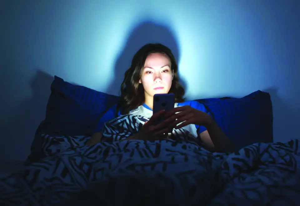 The girl lies at home in the evening on the bed with a phone in the dark.