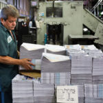 A worker stacks copies of The Coast News at a web offset printing press in Vista in 2018. File photo/Shana Thompson