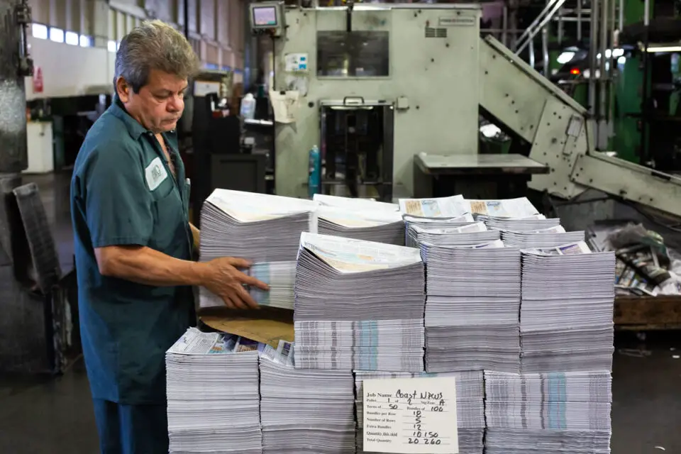 A worker stacks copies of The Coast News at a web offset printing press in Vista in 2018. File photo/Shana Thompson