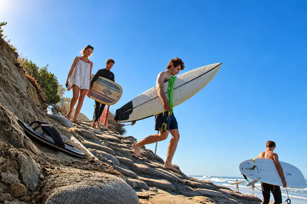 Surfers and beachgoers navigate a steep, eroded shoreline at Beacon's Beach in Leucadia on Oct. 15, 2026. The beach was excluded from a 2024 federal sand replenishment project, prompting renewed efforts to restore sand to northern Encinitas beaches.