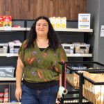 Riham Shenouda, manager of Palomar College's food pantry, stands in front of a shelf in the on-campus resource. Photo by Jim Trageser