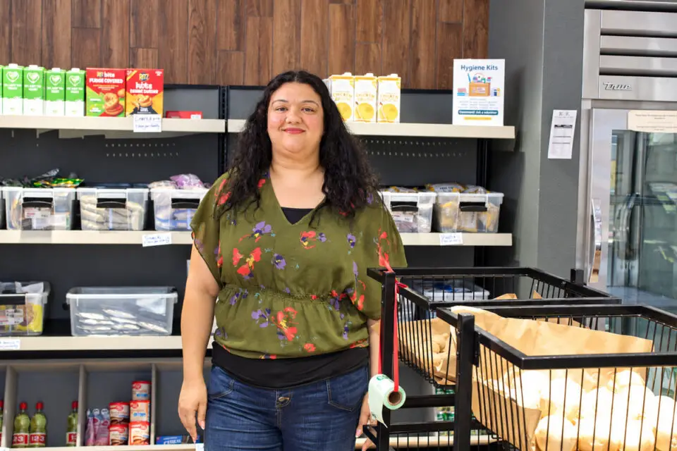 Riham Shenouda, manager of Palomar College's food pantry, stands in front of a shelf in the on-campus resource. Photo by Jim Trageser