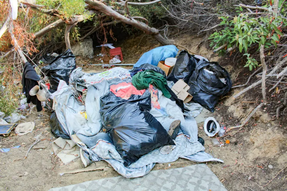 A heap of garbage, including bags of clothes, is just of hundreds of bags of garbage in an homeless camp adjacent to the freeway in Encinitas. Photo by Jordan P. Ingram